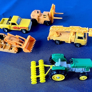 May include: A collection of toy construction vehicles, including a yellow pickup truck, a forklift, a bulldozer, a crane truck, and a green tractor with yellow wheels and a yellow implement. The toys are set against a blue background.