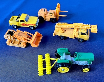 Lotto di 5 veicoli Tomica degli anni '70, carrello elevatore TOYOTA, camion con scala Nissan, bulldozer KOMATSU, camion Chevrolet, trattore KUBOTA, alcuni pezzi di ricambio. Vedi foto.