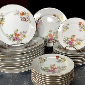 May include: A set of white porcelain dinnerware with a floral pattern in shades of pink, orange, and yellow. The set includes dinner plates, salad plates, and bowls.