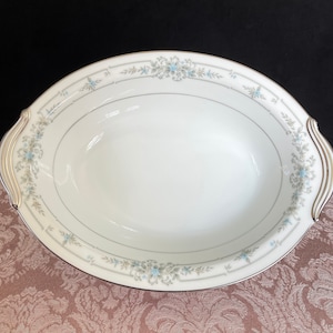 May include: White oval serving bowl with a delicate floral pattern in shades of blue and grey. The bowl has a gold rim and two handles.