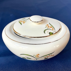 Könnte beinhalten: Cremefarbene Zuckerdose aus Keramik mit Deckel und Goldrand. Der Deckel hat einen kleinen, runden Knopf und ist mit orangefarbenen und grünen floralen Akzenten verziert. Die Schüssel hat ähnliche florale Designs.