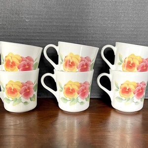 May include: Six white ceramic mugs with a floral design featuring yellow and pink pansies. The mugs are stacked in pairs.