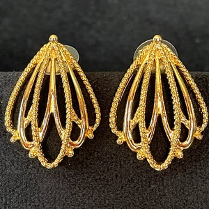 Puede incluir: Un par de pendientes de tono dorado con un diseño delicado e intrincado. Los pendientes tienen forma de abanico o flor con múltiples capas de líneas delicadas e interconectadas.