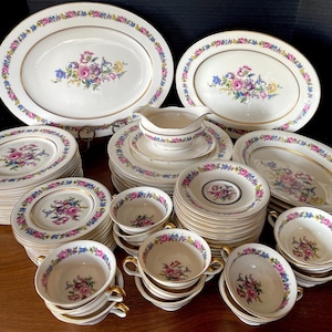 May include: A set of vintage fine china dinnerware with a floral pattern in shades of pink, blue, and green. The set includes plates, bowls, and a serving platter, all with a gold trim.