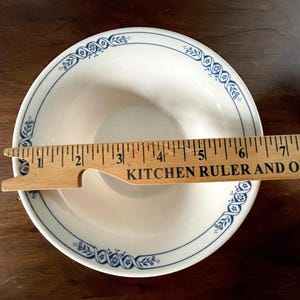 May include: A white ceramic bowl with a blue and white floral design around the rim. The bowl is 12.7 cm in diameter.