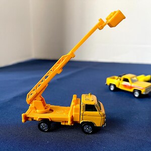 May include: A yellow toy truck with an extending crane arm. The crane arm is raised, and the truck has black wheels. Other toy vehicles are visible in the background.