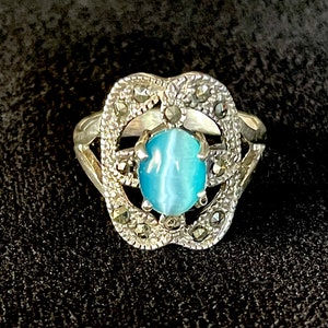May include: A silver ring with a blue cat's eye stone set in a filigree design with marcasite accents.