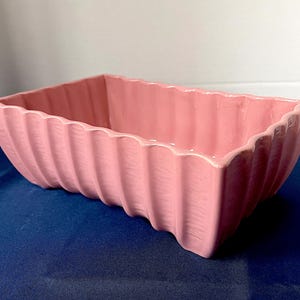 May include: A rectangular, pink ceramic planter with a ribbed exterior. The planter has a scalloped rim. The dimensions are approximately 30 cm long, 15 cm wide, and 10 cm tall. Suitable for indoor or outdoor use.