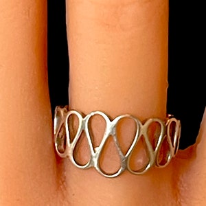 May include: A silver ring with a delicate, openwork design featuring a repeating pattern of connected ovals.