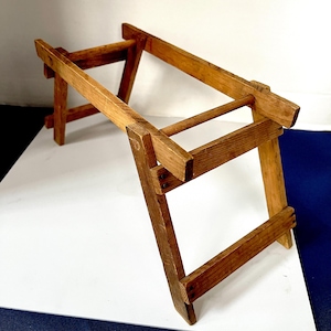 Könnte beinhalten: Ein kleiner, zusammenklappbarer Holztritt mit natürlichem Finish. Der Tritt hat zwei Stufen und ist aus rechteckigen Holzbalken und Dübeln gefertigt. Die Beine sind für Stabilität abgewinkelt. Misst ca. 46 cm lang, 30 cm breit und 38 cm hoch.