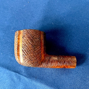 May include: A brown, L-shaped tobacco pipe with a textured surface. The pipe has a dark brown bowl and stem, with a lighter brown accent on the side. The pipe is made of wood.