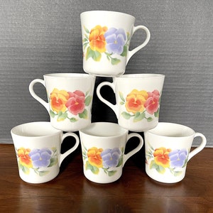 May include: Six white ceramic mugs with handles, each featuring a different floral design with yellow, purple, red, and orange pansies.