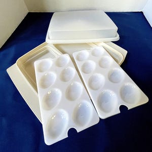 Könnte beinhalten: Ein Set aus cremeweißen Kunststoff-Malpaletten mit ovalen Vertiefungen, einer rechteckigen Schale und einem passenden Deckel. Die Paletten sind zum Mischen von Farben konzipiert.