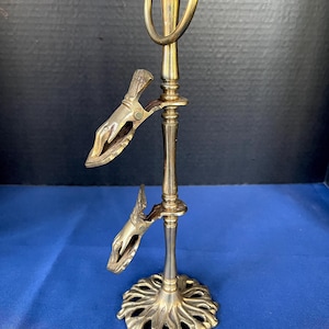 Puede incluir: Un soporte de servicio vintage en tono latón con dos pinzas con resorte y un asa de anillo. La base tiene un diseño floral decorativo. El soporte mide aproximadamente 25 cm de alto.