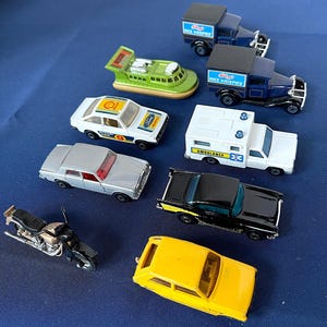 以下が含まれることがあります： バイク、黄色い車、黒い車、シルバーのセダン、白い救急車、"Rice Krispies"ブランドの青いトラック2台、白と青のフォード車、緑色のホバークラフトなど、おもちゃの車のコレクション。