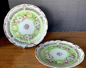 AQ Three Crowns Porc Plts Verdes con rosas estampadas en rosa, blanco y amarillo. Ribete dorado aplicado a mano. Base blanca, detalles blancos en relieve. Sin desgaste ni daños.