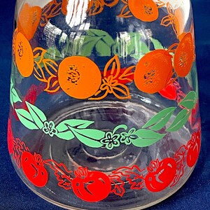 May include: Clear glass pitcher with a wide base and a narrow neck. The pitcher is decorated with orange, green, and red fruit and floral designs. The fruit appears to be oranges and tomatoes. The pitcher is likely vintage.
