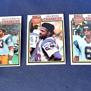 May include: Three vintage football trading cards featuring players from the Chargers. Each card has a player's name and position, with team colors of powder blue, yellow, and white. The cards are on a blue background.