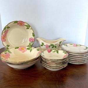 Può includere: Un set di piatti in ceramica vintage con motivo floreale, che comprende una grande ciotola da portata, una ciotola più piccola, una salsiera e un set di ciotole più piccole. I piatti presentano un motivo floreale rosa e verde su sfondo bianco.