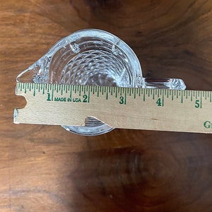 Op de afbeelding: Een glazen kan met een transparante, getextureerde oppervlakte. De kan is ongeveer 7,5 cm breed en 10 cm hoog. De kan staat op een houten oppervlak.