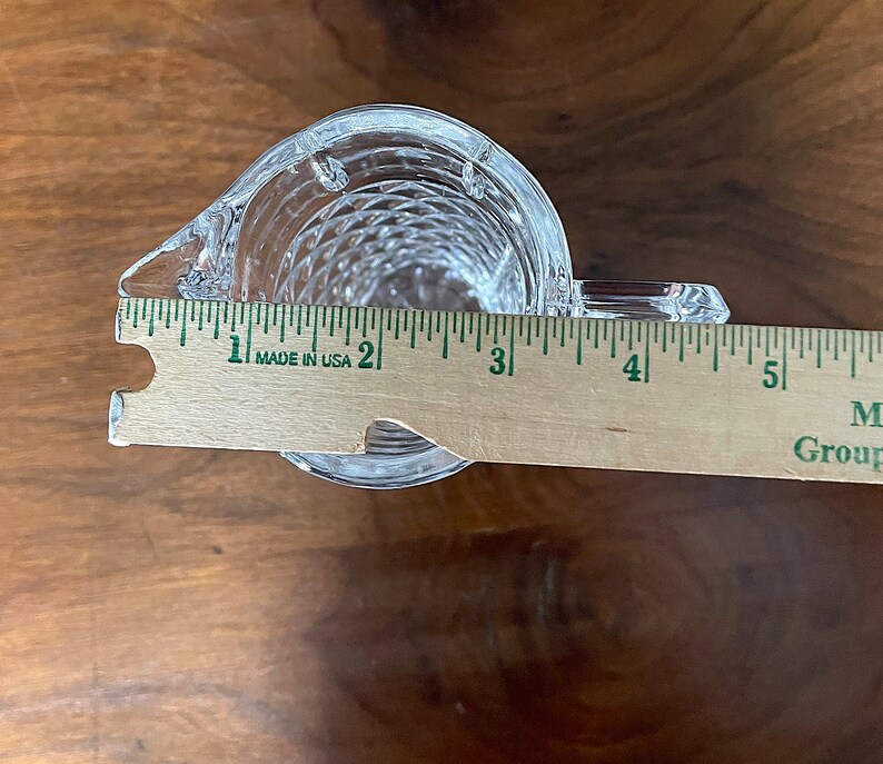 Op de afbeelding: Een glazen kan met een transparante, getextureerde oppervlakte. De kan is ongeveer 7,5 cm breed en 10 cm hoog. De kan staat op een houten oppervlak.