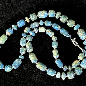 May include: A necklace with blue and green stone beads of different sizes. The beads are strung with small silver-coloured spacers and a silver-tone clasp. The necklace is shown against a black background.