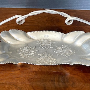 May include: A silver serving tray with a twisted wire handle. The tray has a scalloped edge and a floral design.