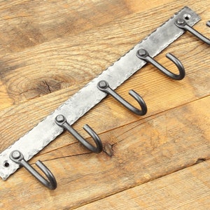 May include: A metal wall-mounted hook rack with five hooks. The rack is made of hammered metal and has a rustic finish. The hooks are all in a row and are evenly spaced.