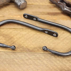 Pair of hand forged iron curtain tie back hook, ball end style, natural iron color, on a rustic background.