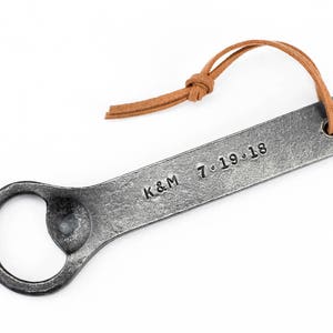 Customized hand forged iron bottle opener with a leather tassel on a white background.
