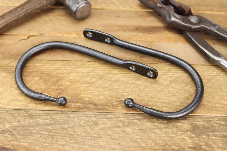 Pair of hand forged iron curtain tie back hook, ball end style, natural iron color, on a rustic background.