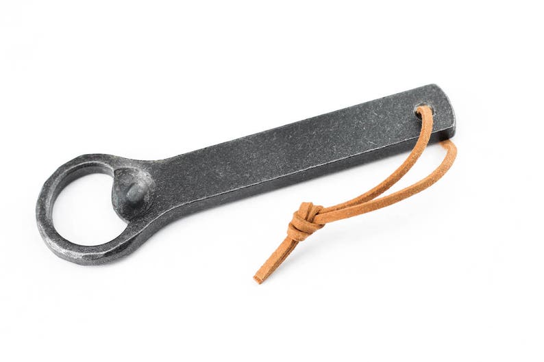 A grey blacksmith made iron bottle opener with a light brown leather tassel on a white background.