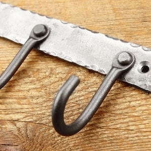 May include: A metal wall-mounted hook rack with three hooks. The rack is made of hammered metal and has a rustic finish.