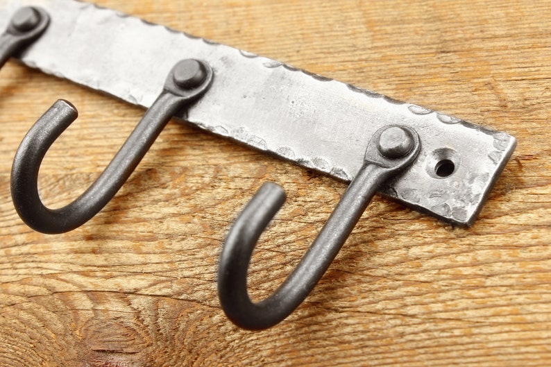 May include: A metal wall-mounted hook rack with three hooks. The rack is made of hammered metal and has a rustic finish.