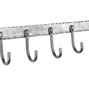 May include: A silver metal wall-mounted hook rack with five hooks. The rack has a hammered finish and is designed for hanging items.