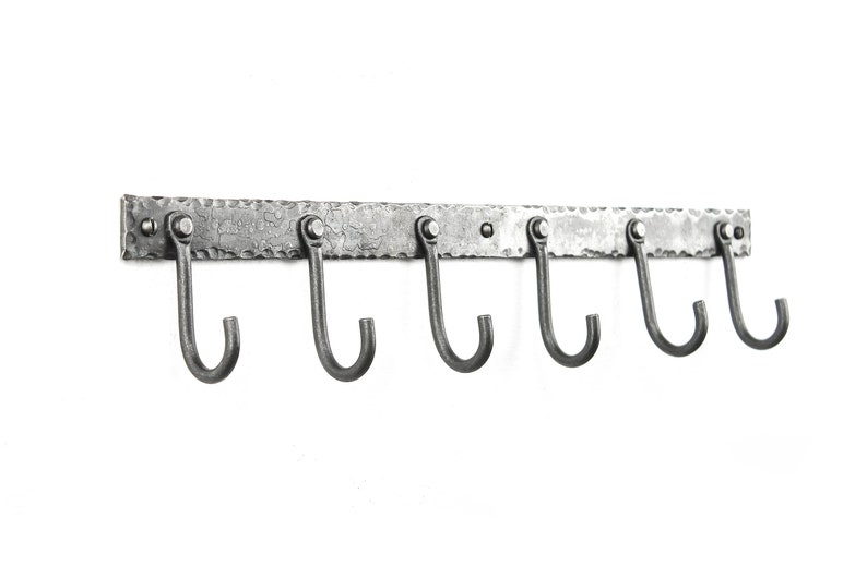 May include: A silver metal wall-mounted hook rack with six hooks. The rack has a hammered texture and is designed for hanging items.