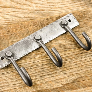 May include: A metal wall-mounted hook rack with three hooks. The rack is made of hammered metal and has a rustic finish.