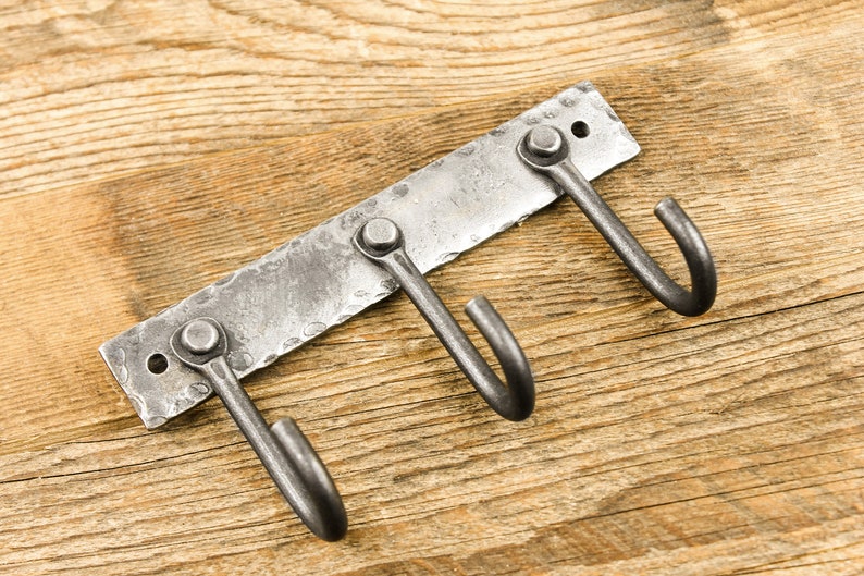 May include: A metal wall-mounted hook rack with three hooks. The rack is made of hammered metal and has a rustic finish.