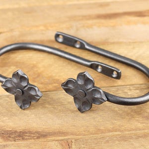A pair of blacksmith made iron curtain tie back hooks, Flower style, on a rustic background.