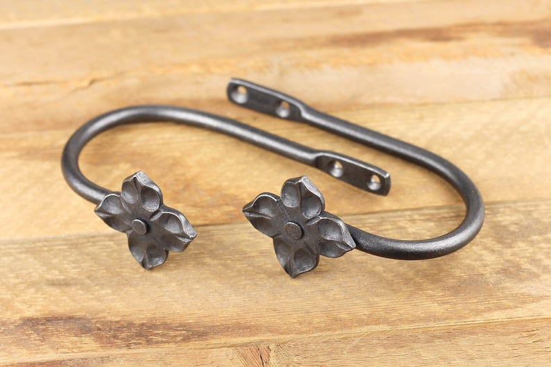 A pair of blacksmith made iron curtain tie back hooks, Flower style, on a rustic background.