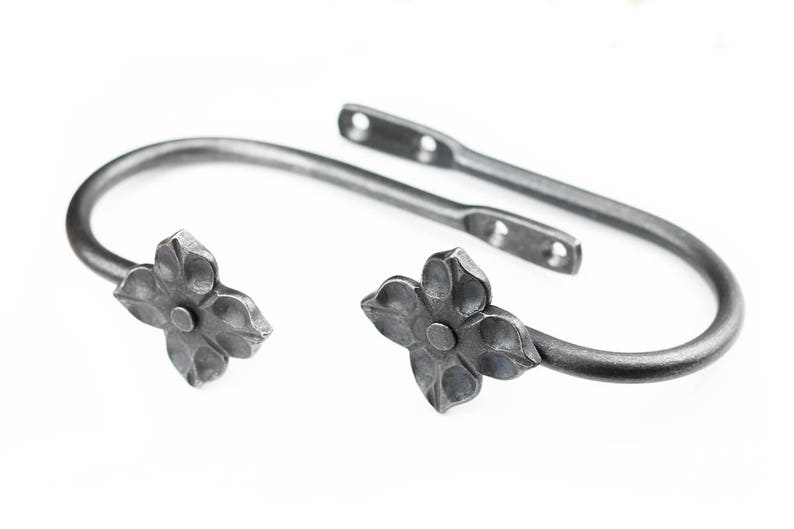 A pair of Hand forged iron curtain tie back hooks, Flower style, on a white background.