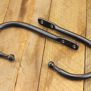 Pair of hand forged iron curtain tie back hook, ball end style, natural iron color, on a rustic background.