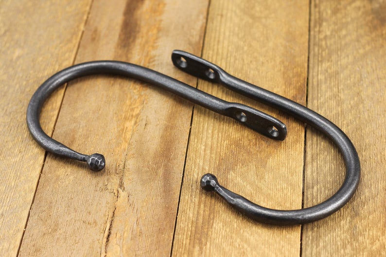 Pair of hand forged iron curtain tie back hook, ball end style, natural iron color, on a rustic background.