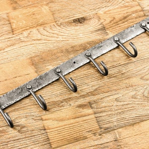 May include: A metal wall-mounted hook rack with six hooks. The rack is made of hammered metal and has a rustic finish. The hooks are curved and are ideal for hanging keys, coats, or other items.