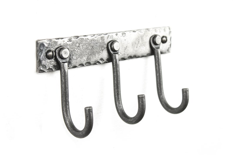 May include: A silver metal wall mounted hook rack with three hooks. The rack has a hammered texture and is mounted with three screws.
