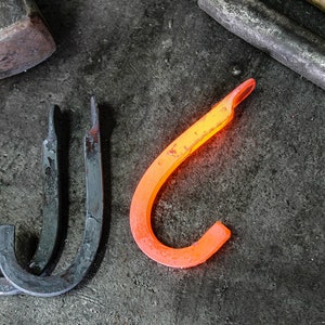 May include: Three metal hooks, two are black and one is glowing orange, on a dark gray surface.