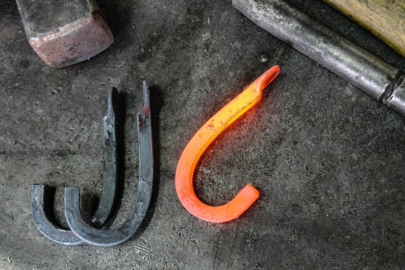 May include: Three metal hooks, two are black and one is glowing orange, on a dark gray surface.