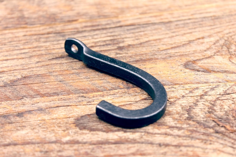 May include: A black metal hook with a rounded end. The hook is lying on a wooden surface.