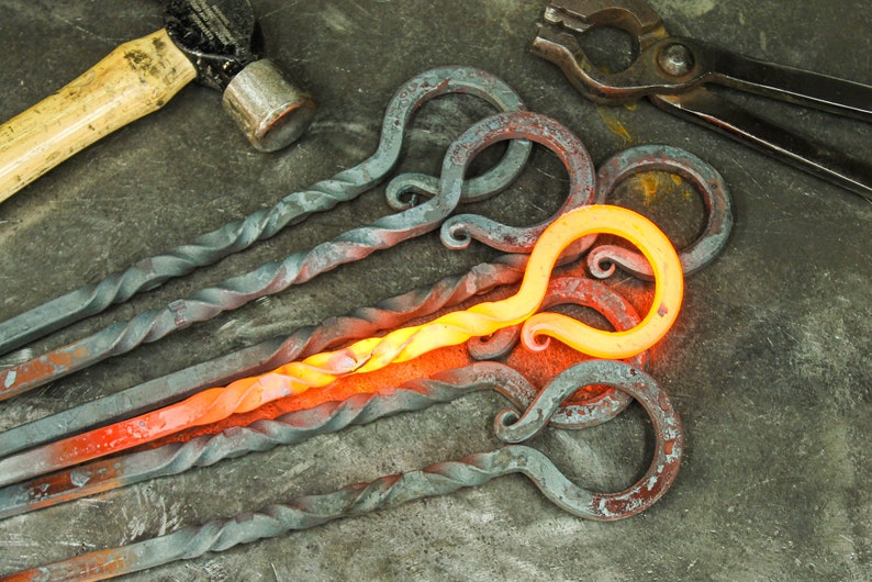 Hand forged iron fire poker twisted handles on a rustic metal table.