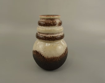 May include: A ceramic vase with a unique design. The vase features a bulbous base and a cylindrical neck with stacked, ring-like details. The color scheme includes shades of brown, cream, and a touch of red at the rim. The base has a textured, rough surface.